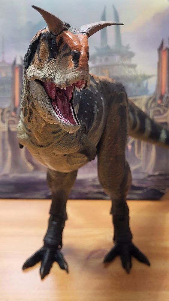 Front shot of the Carnotaurus posed like the package art by Raph Lomotan, in front of the background insert (artwork side)